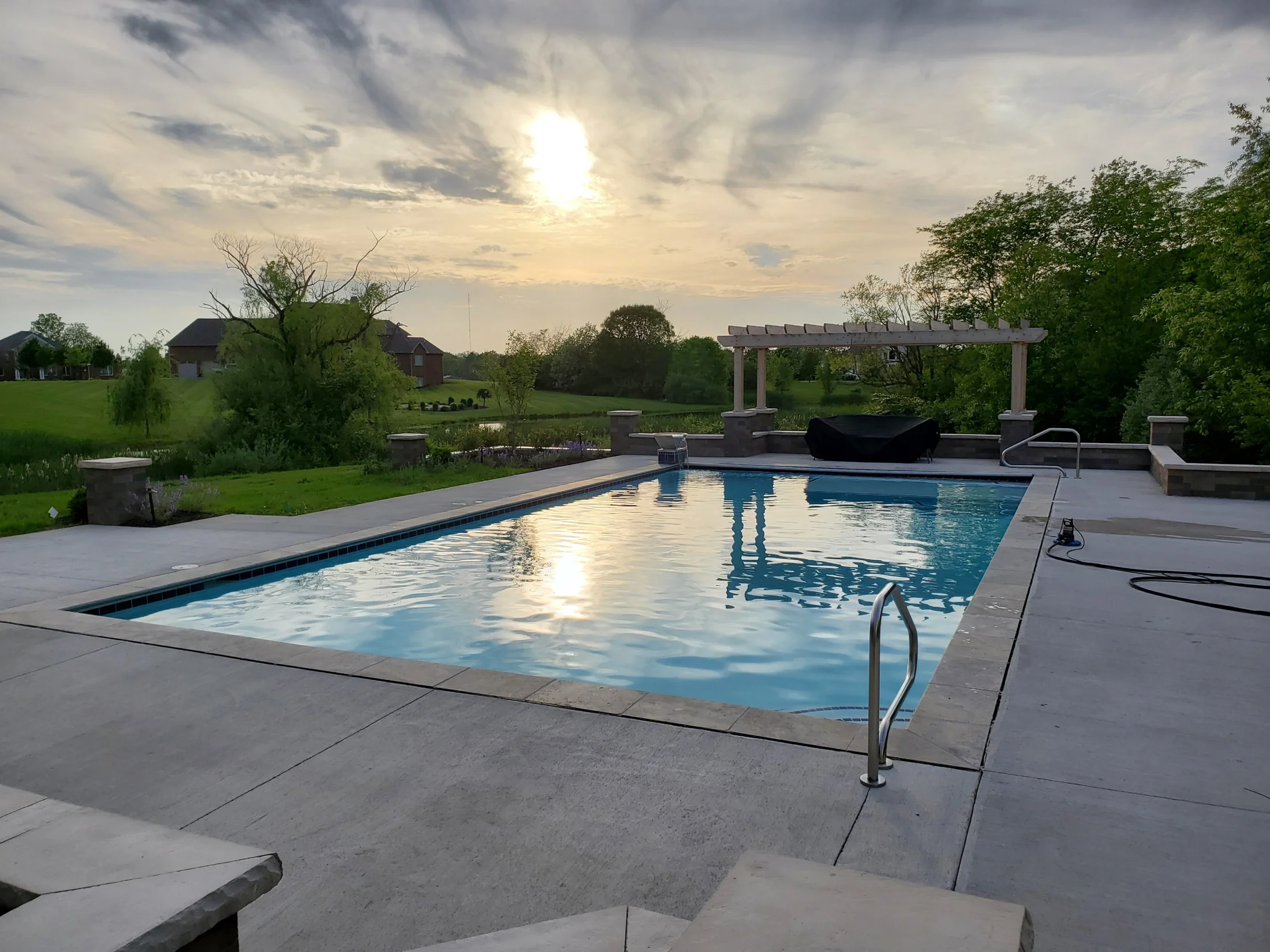 Gunite pool at sunset with a broad deck, lawn, and pergola