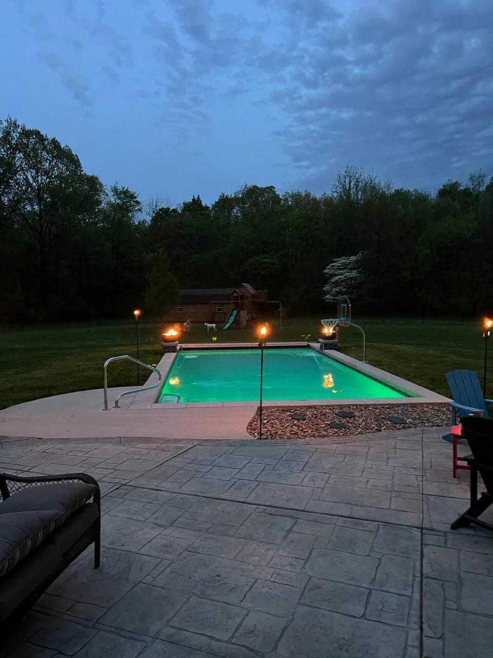 Illuminated vinyl liner pool at dusk with an open surrounding patio